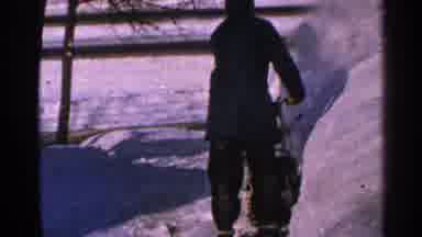 Minnesota USA (1965): Man Wearing Black Snowsuit Uses Snowblower On A Clear Winter