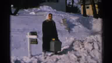 Minnesota USA (1965): A Woman Stands On The Bank Of Shoveled Snow Beside A Mailbox