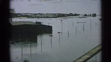 Minnesota USA (1965): Debris Litters The Flooded Waterway That Borders A Town