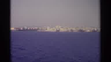 Sicily-1965: Boat Journey Past Coastal Town With Blue Sea And White Buildings