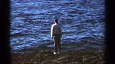 Hamel Minnesota (1966): Man Wearing Grey Pants Stands Looking At Water On A Sunny