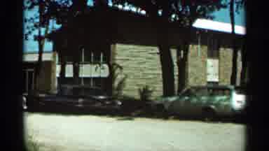 Hamel Minnesota (1966): White Car Parked By Brown Building On A Bright Sunny Day