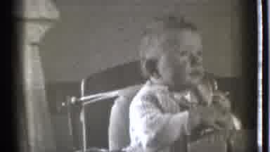Danielson Connecticut (1939): Baby Wearing White Shirt Sits In Highchair Smiling
