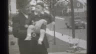 New York (1939): Man Wearing Black Cot Holds Toddler And Points At Comer