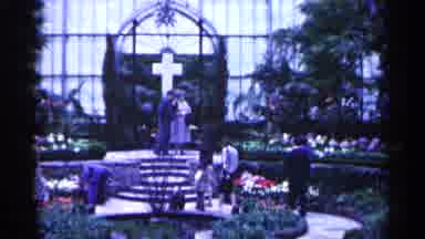 Minnesota USA (1961): People Walking Round A Endothermic Garden With Cross In