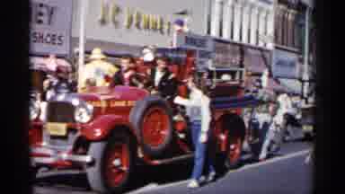 Minnesota USA (1961): Cars Driving Down Road With People Marching Behind It
