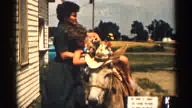 Colorado USA (1963): Child Being Helped Onto Donkey Wearing Hat By Woman On Side