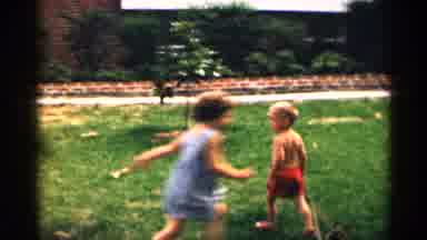 Texas USA (1963): Three Small Children Run Round And Ply In Yard On Lively Summer
