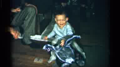 New York (1955): Young Child Wearing Poms Sits On Toy And Smiles While Looking