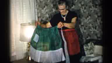 New York (1955): Woman Wearing Black Dress Holds Up Green Pron Next To Christmas