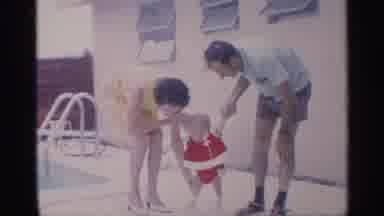 Florida (1959): Couple Helps Toddler Wearing Red Shirt To Sand While Woman Wearing