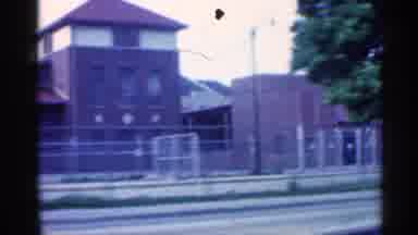 Indiana (1959): Vehicle Traveling Down City Street Past Buildings And Champion