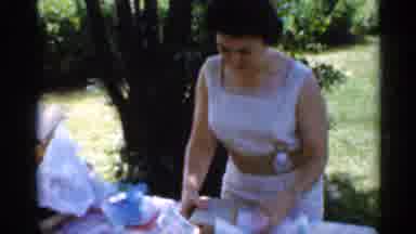 Indiana (1959): Woman Unwraps Presents On Picnic Table One Tree In Lawn Of Green