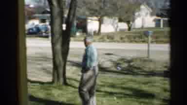 Indiana (1959): Man Walks On Grass Outside While Inside Woman Cooks And Man Smiles