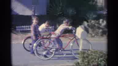 Indiana-1959: Two Kids Race On Red Bicycles In Street On Bright Sunny Day