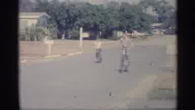 Indiana (1959): Two Boys Riding Bikes Racing In Middle Of Residential Street On