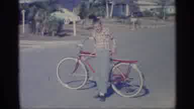 Indiana (1959): Boy Wearing Green Ants Gets On Red And Yellow Bicycle On Cleo Day