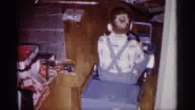 Michigan (1959): Boy Wearing Blue Pants Drives Toy Blue Car Across Wooden Floor