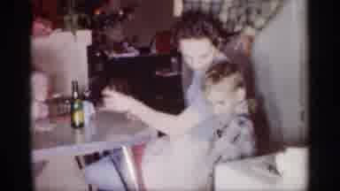 Michigan (1959): Woman Wearing Blue Dress Drinks From Clear Cup While Sitting At