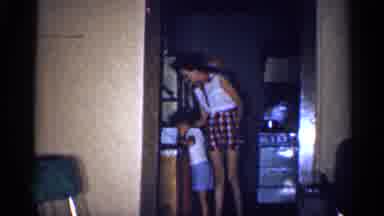 Michigan (1959): Woman Wearing White Shirt Places Small Object On Kitchen Table