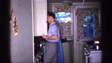 Michigan (1959): Man In Blue Business Attire Opens A Cabinet Then Camera Pans To