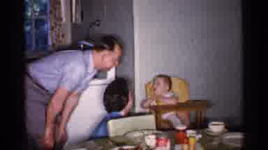 Michigan (1959): Man Wearing Blue Shirt Talks To Baby Sitting In Yellow Highchair