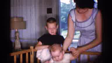 Michigan (1959): Woman In Blue And White Dress Lifts Baby Out Of Crib
