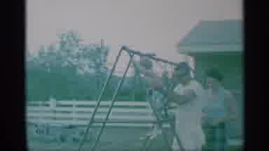 New York (1959): Man Wearing White Shirt Lifts Toddler From Swing Set On A Clear