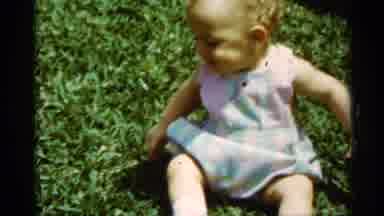 Mississippi (1963): Baby In Green And Pink Dress Sits On Grass Looking Confused