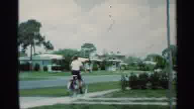 Mississippi (1963): Boy Wearing White Shirt Rides Red Bicycle Down Sidewalk While