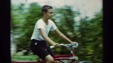 Mississippi (1963): Boy Wearing White Shirt Rides Red Bicycle On A Sunny Day