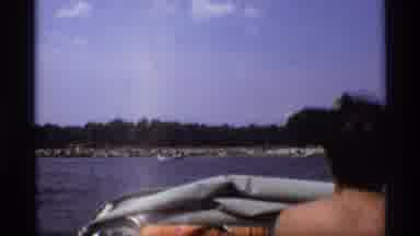 New York (1973): Man Drives Boat On Lake Near Beach While People Swim In Water