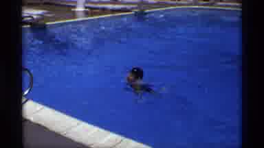 New York (1973): Boy Wearing Black Shorts Swims To Side Of Pool On A Bright Sunny
