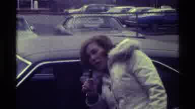 Kentucky (1976): Woman Wearing White Coat Talks To Person In Car Through Window On