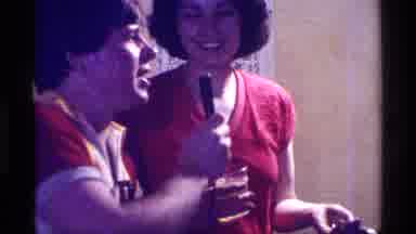 Kentucky (1976): Man Wearing Red Shirt Holds Microphone Up To Woman Wearing Black