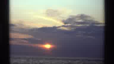 Holland Michigan (1969): Gold Sun Setting Behind Grey Clouds Over Calm Lake Water
