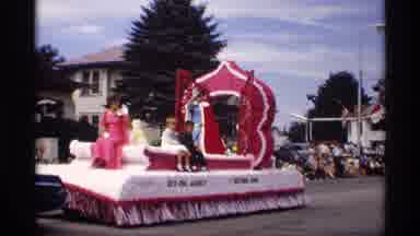 Mabel Minnesota (1969): Woman Wearing Red Dress Rides On Red Parade Float On A