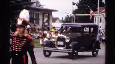 Mabel Minnesota (1969): Woman Wearing White Dress Waves To Crowd From Brown Parade