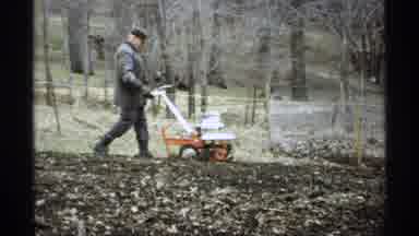 La Crosse Wisconsin (1971): Man Wearing Grey Coat Tills Garden Soil On A Cloudy