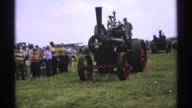 Minnesota (1971): People Look As Others Drive Tractors Through The Grass In Show