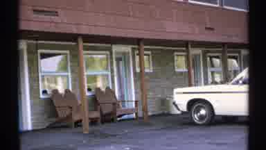 New York (1971): Pair Of Brown Wooden Chairs Sitting Next To Parked White Vehicle
