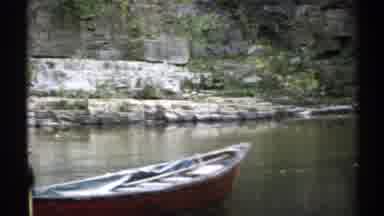 New York (1971): Person Wearing Grey Jacket Rows Brown Rowboat In Pond On A Clear