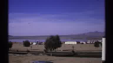 Arizona (1972): Black Car Travels Down Near Empty Road On A Sunny Day