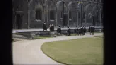 England (1949): People Wearing Black Robes Climb Up Stone Stairs On A Cloudy Day