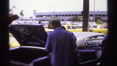 La Paz Mexico (1974): Man Adjusts Red Jacket Standing Next To Open Car Trunk On A