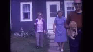 Chicago Illinois (1972): Man Walks Towards The Camera While Holding A Cat As Two