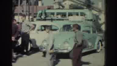 RHODES GREECE-1962: Men Gather Around Blue Volkswagen Beetle and White Car