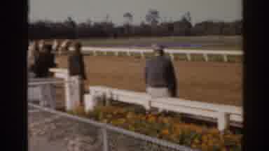 Florida USA (1962): Onlookers Watch A Group Of Horses Rid By Jockeys On A Dirt