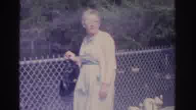 Florida USA (1962): Older Lady Standing Outside Near A Fence And Under A Stone