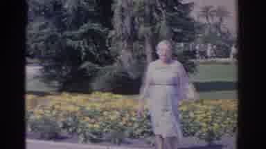 Florida USA (1962): Woman Wearing Blue Dress Stands In Front Of Yellow Flower Bed